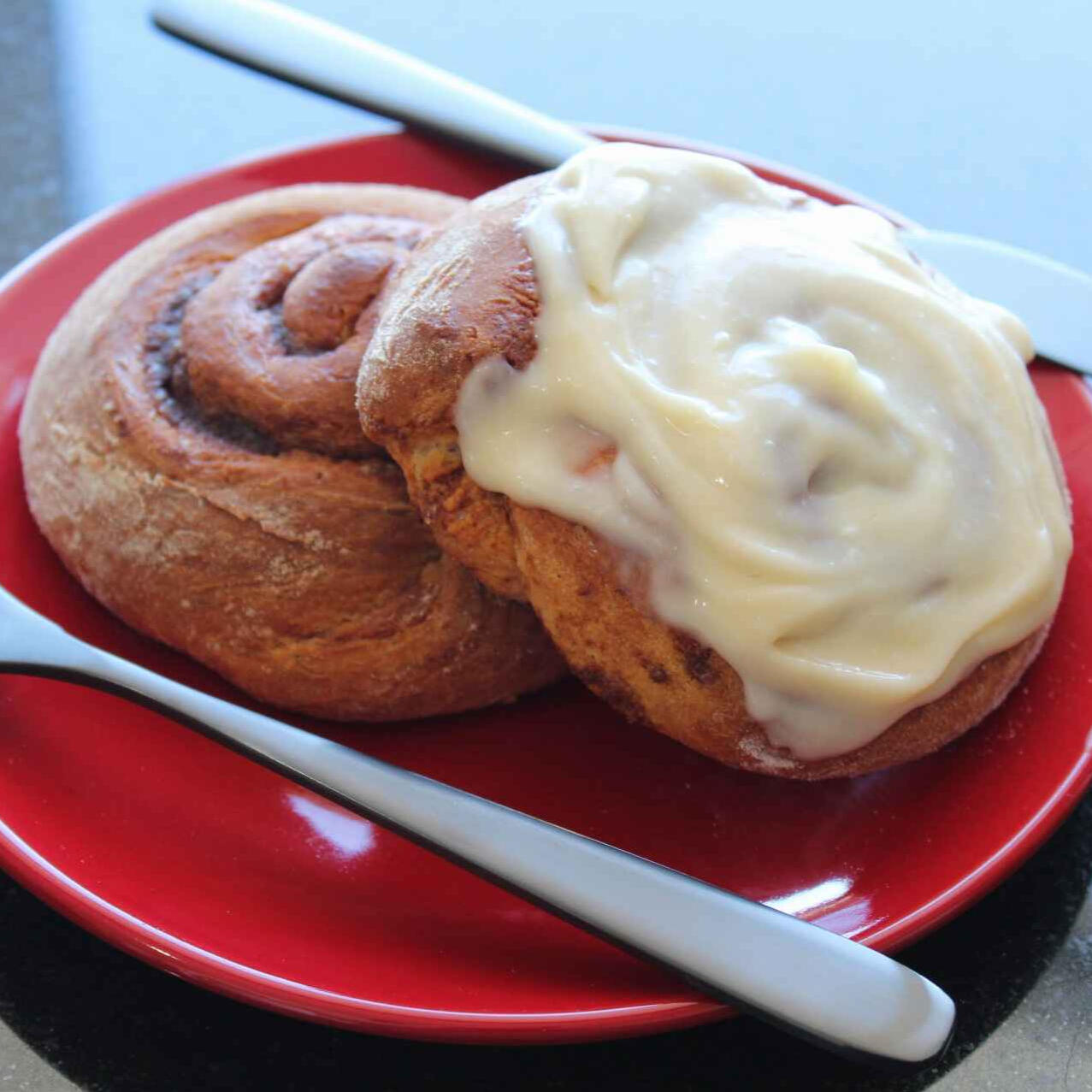 A photo of two cinnamon rolls on a red plate, one of them has white frosting on it.