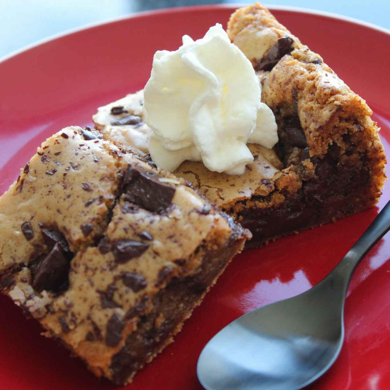 A photo of two chocolate chip cookie bars topped with whipped cream on a red plate.