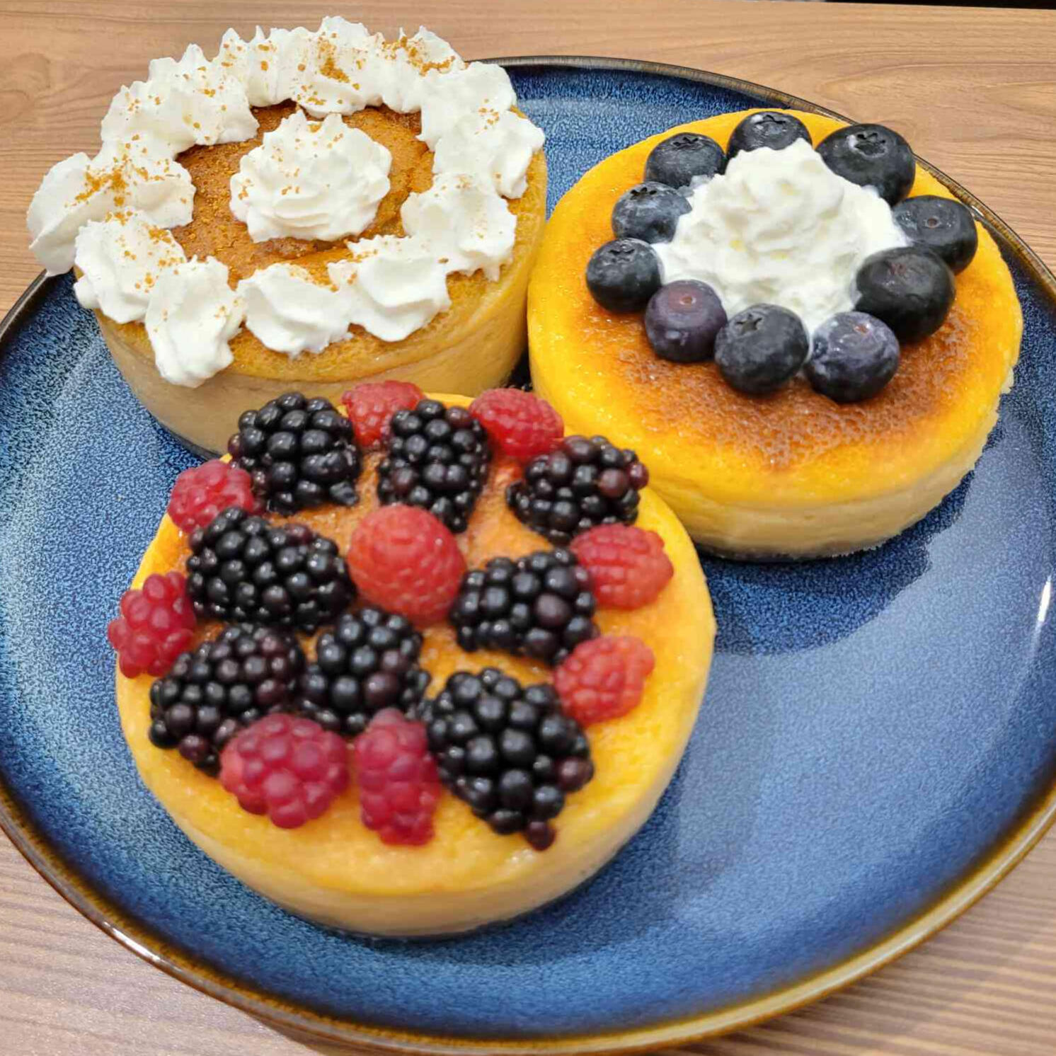 A photo of three cheesecakes, the left one being pumpkin spice, the right blueberry, and the bottom raspberry and blackberry.
